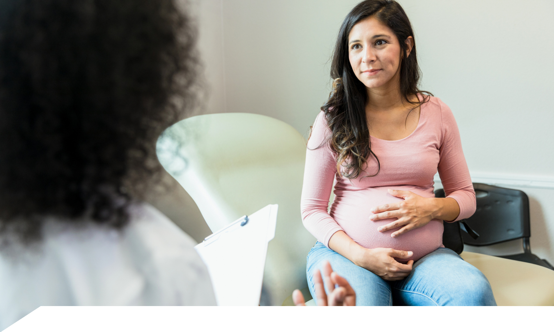 A woman with her hand over her pregnant belly facing her doctor