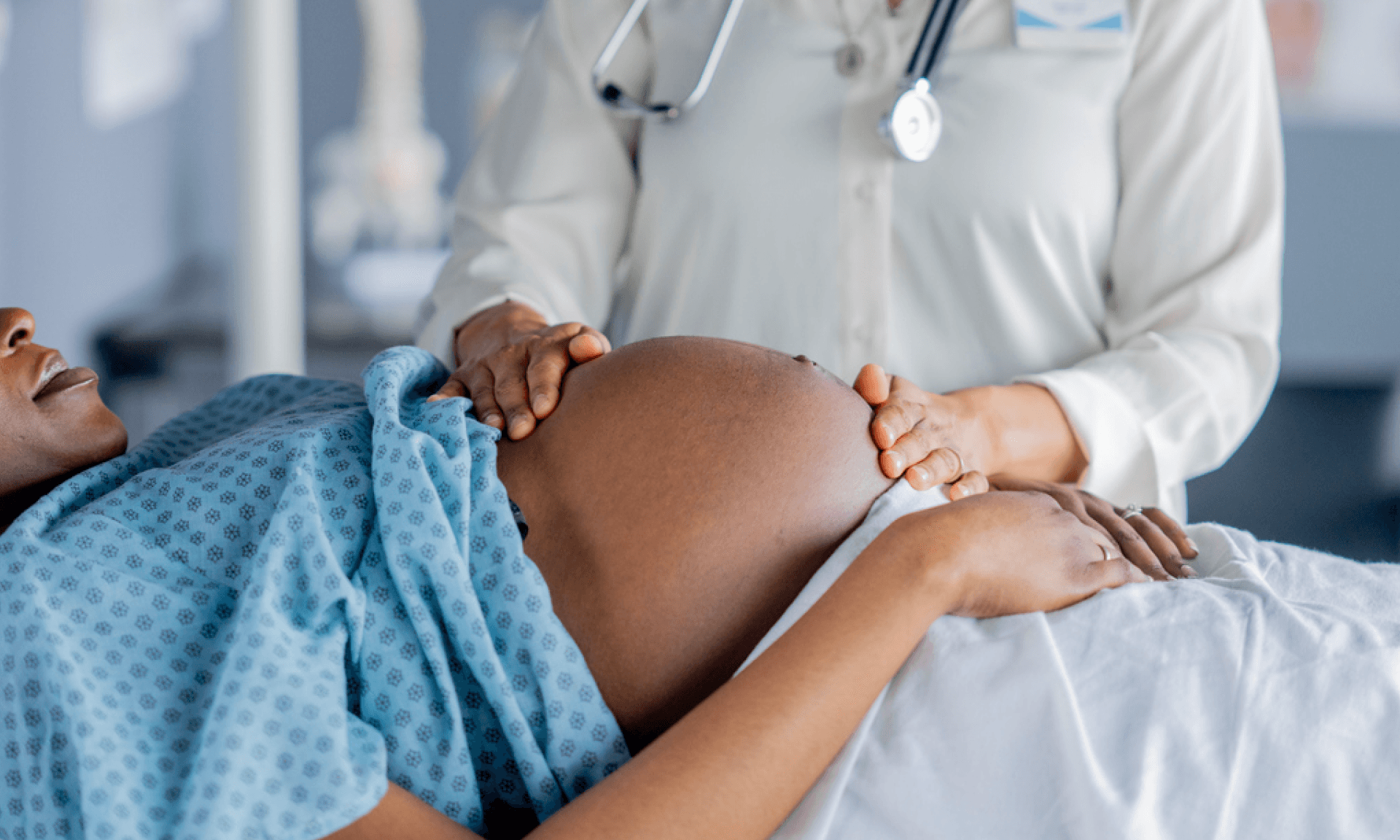 A pregnant woman on a hospital table with a doctor's hands on her stomach