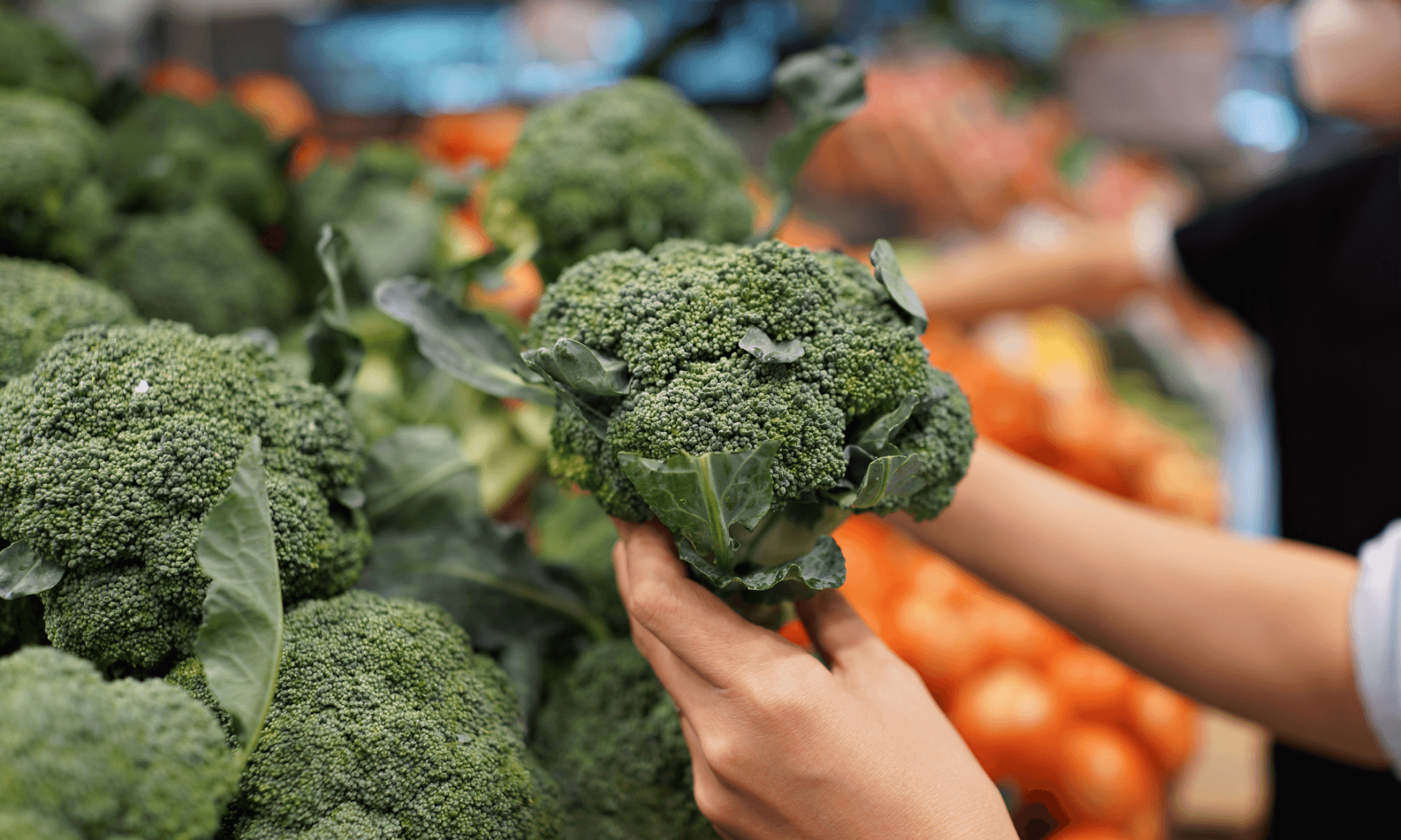 A person holding a head of broccoli at the grocery store